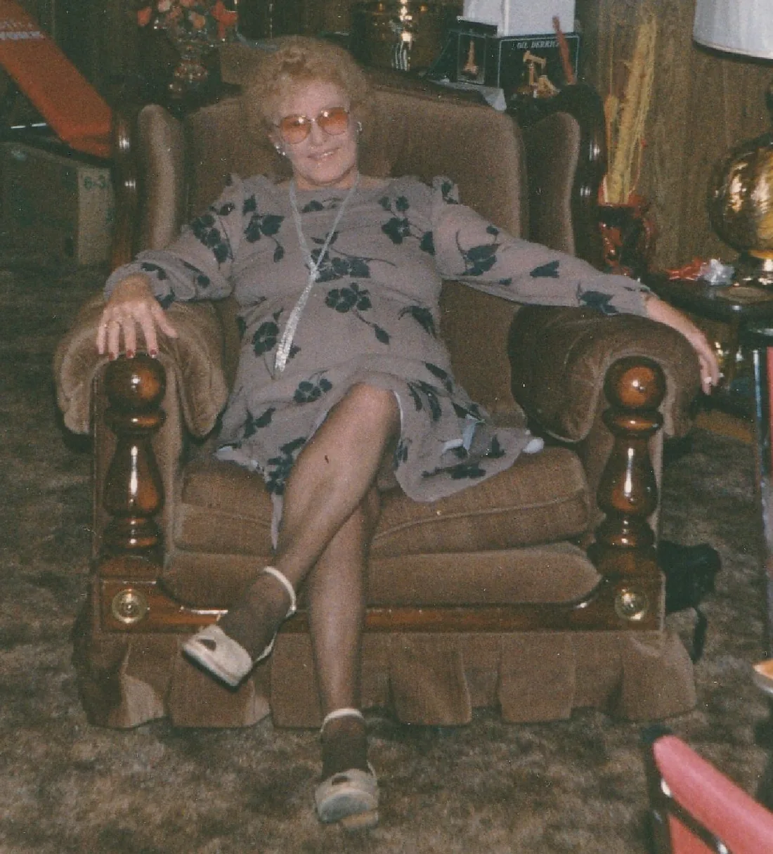A faded, grainy photograph of a woman seated in an armchair in a living room.