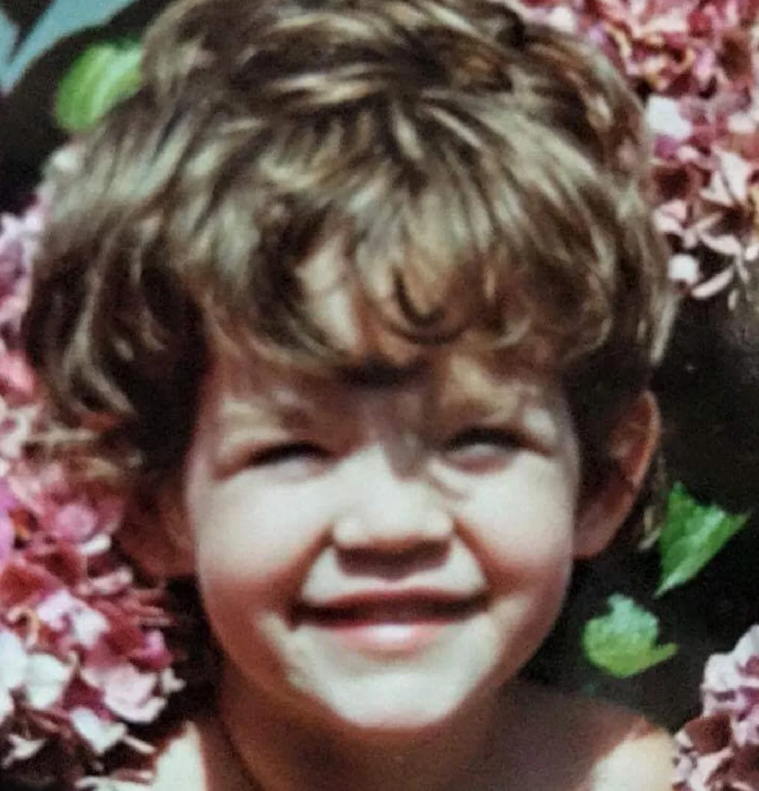 A soft, flat photograph of a smiling child in front of blossom.