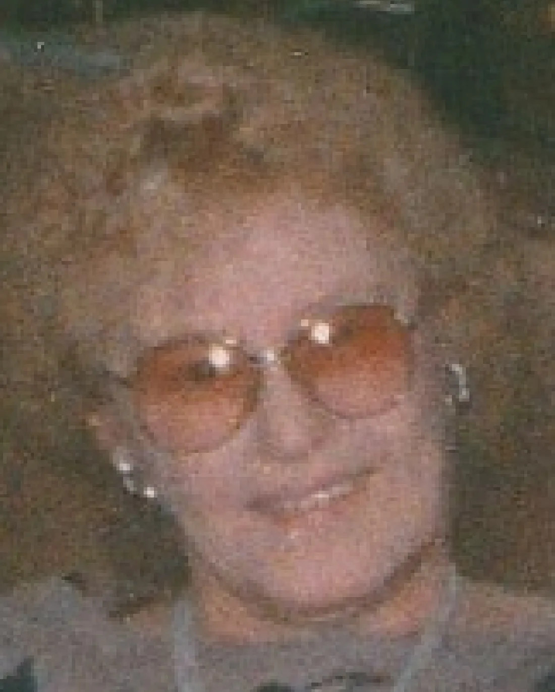A portrait of a woman in tinted glasses, heavily speckled with grain and washed out.